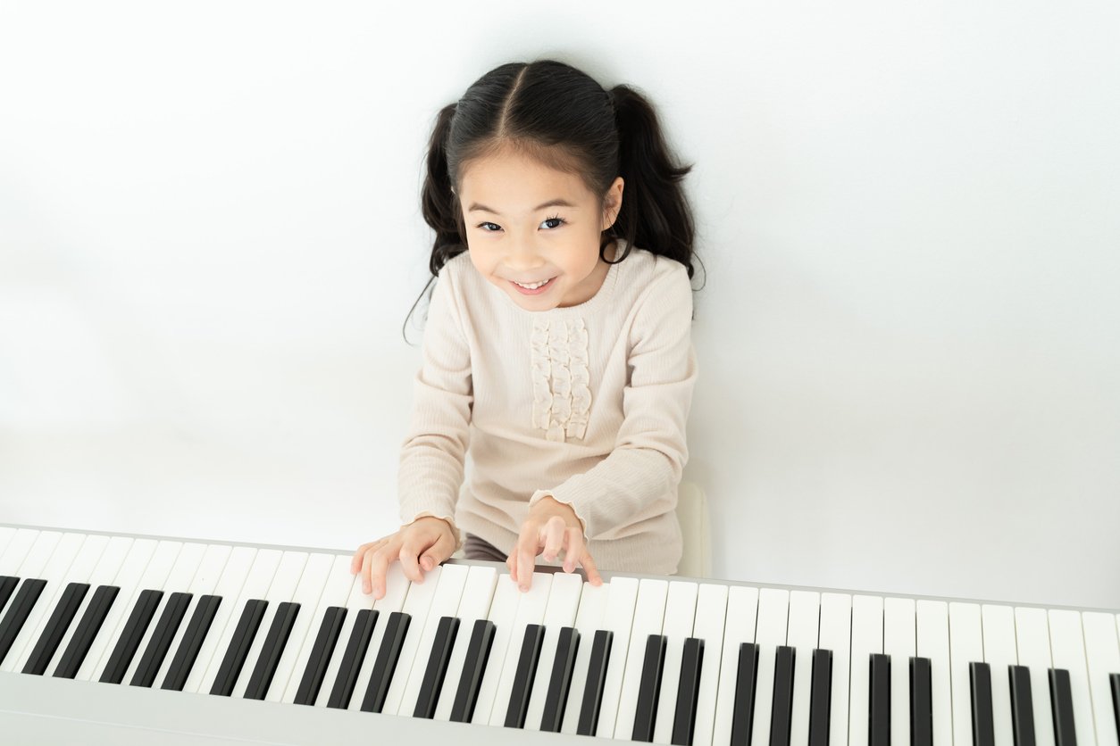 happy asian preschooler playing piano in house